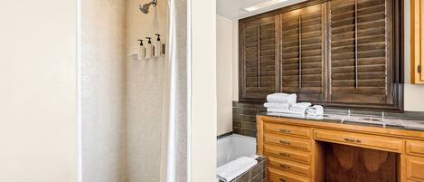 A bathroom with a shower, a bathtub, and a vanity with a large mirror and wooden cabinets.