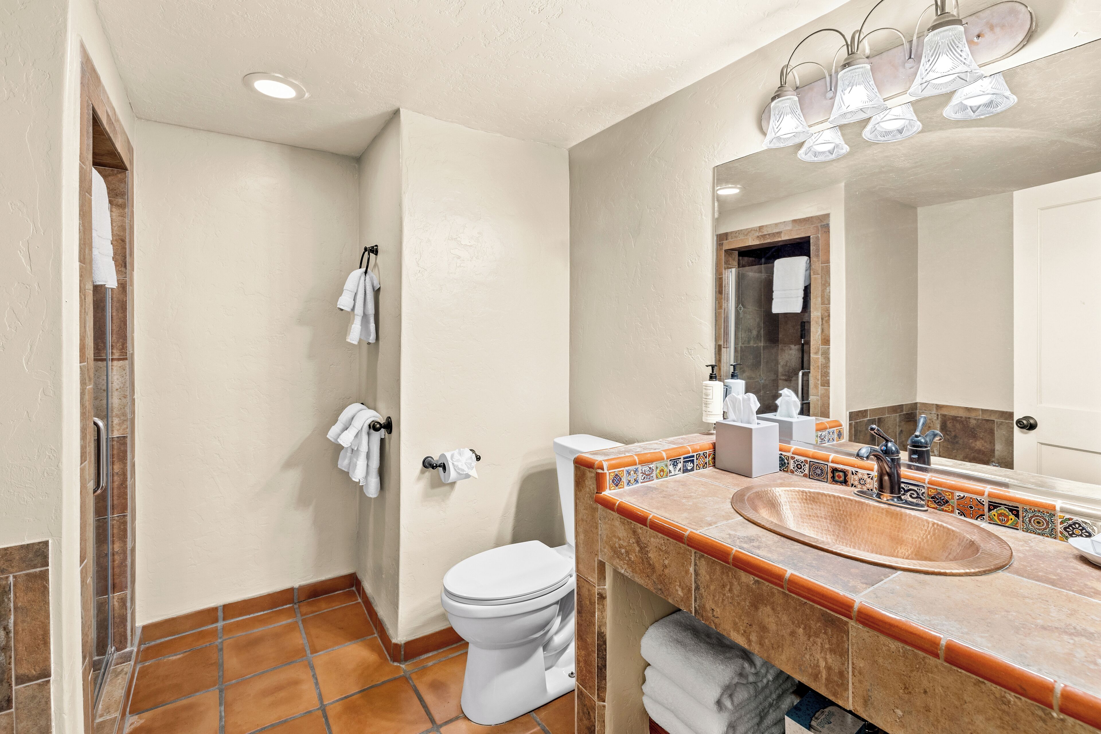 A bathroom with a white toilet, a sink with a copper basin, and a mirror with lights.