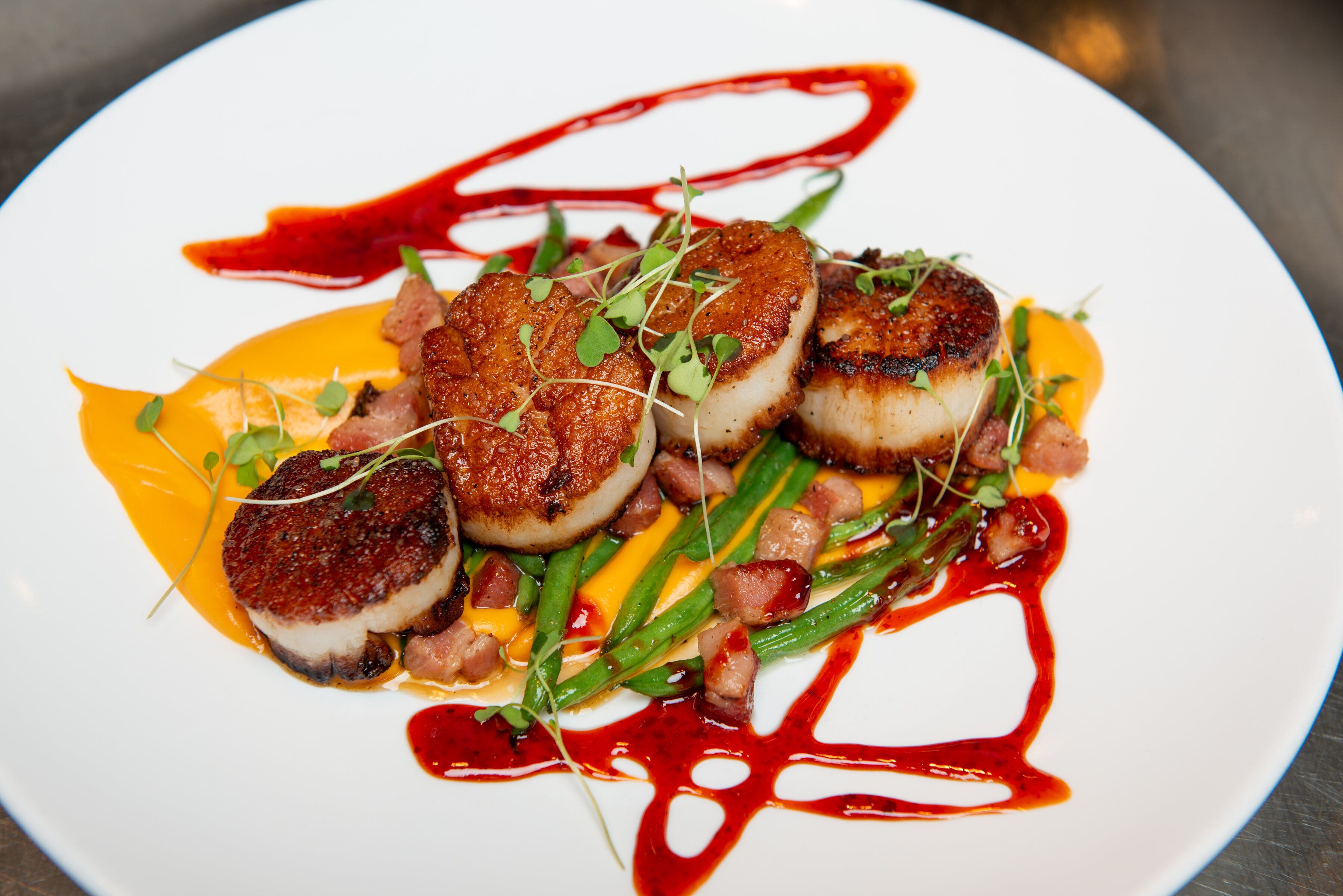 A plate of food with seared scallops, green beans, and a red sauce.