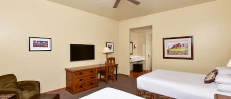 A hotel room with two beds, a desk with a chair, a television, and framed pictures on the walls.