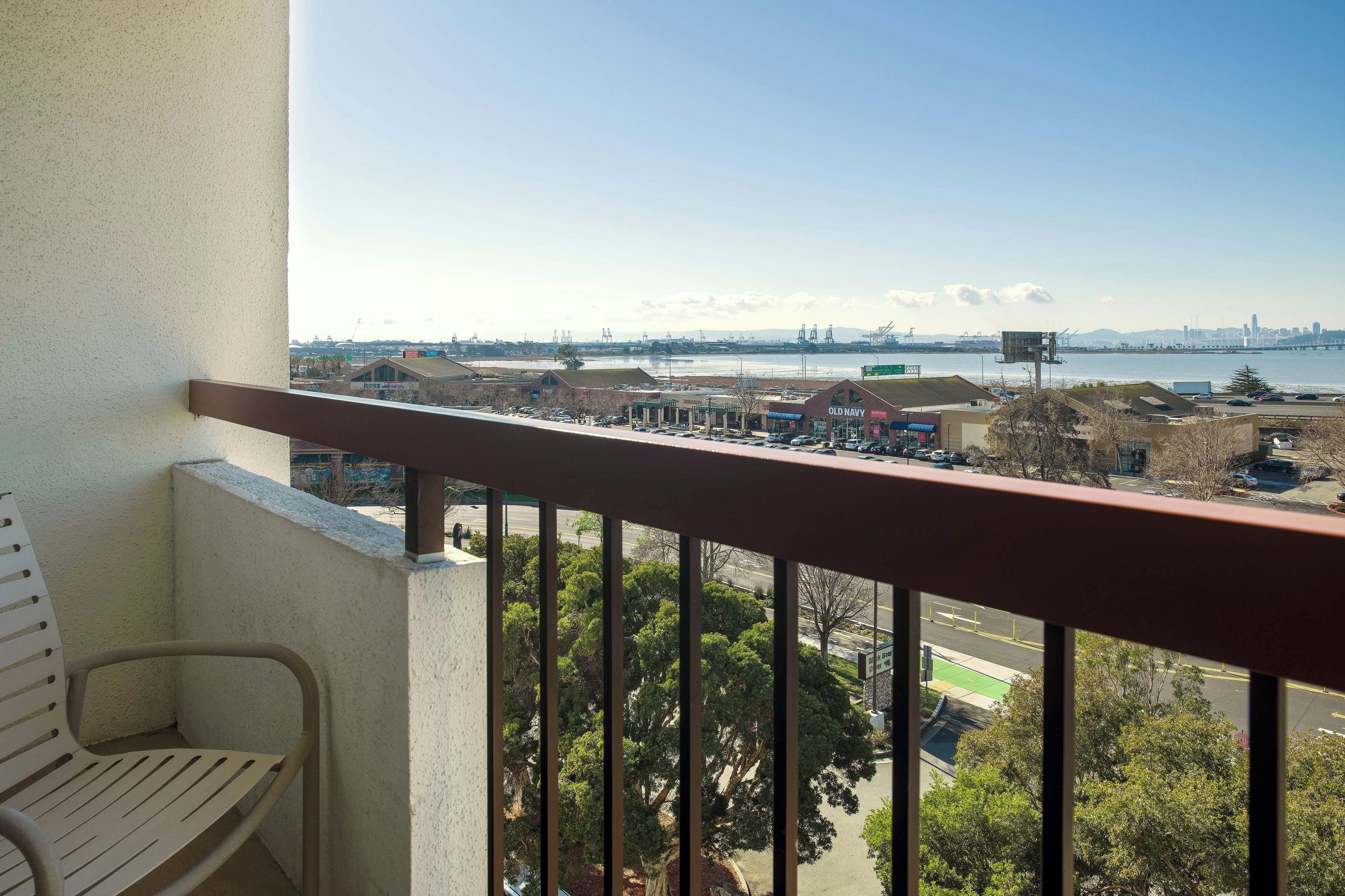 A balcony with a view of a commercial area, including a parking lot and a bridge.