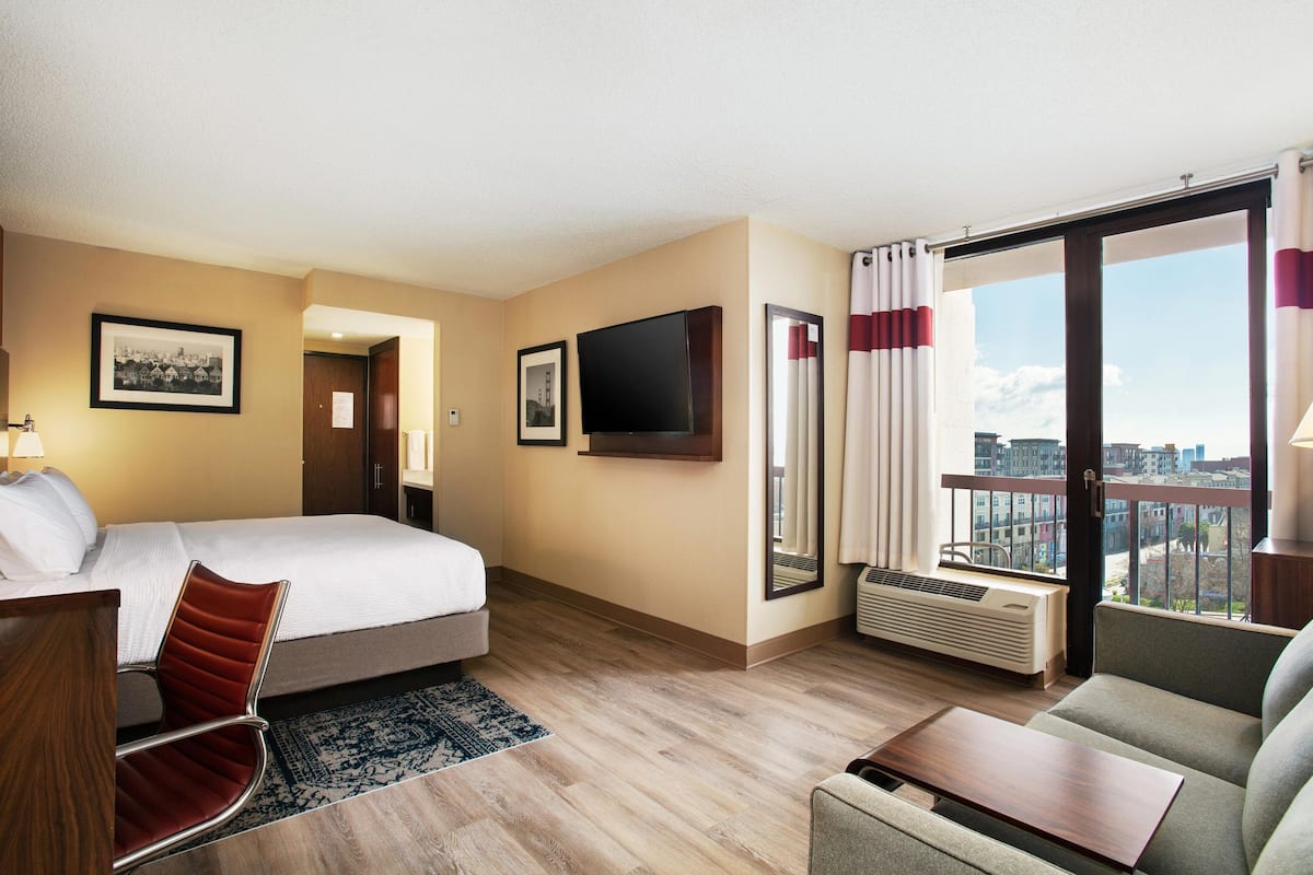 Ein Hotelzimmer mit Bett, Sofa, Schreibtisch, Fernseher und einem großen Fenster mit Blick auf die Stadt.