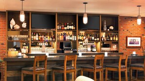 A bar area with wooden chairs, a bar counter, and shelves stocked with bottles and glasses.