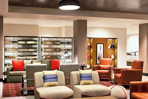 A modern lounge area with sofas, armchairs, a bookshelf, and a view of a bridge. - Four Points by Sheraton San Francisco Bay Bridge (Emeryville)