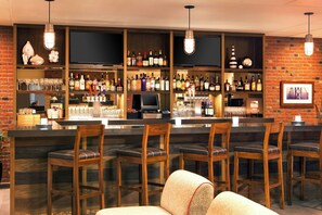 A bar area with multiple seating options, a variety of liquor bottles, and a television screen. - Four Points by Sheraton San Francisco Bay Bridge (Emeryville)