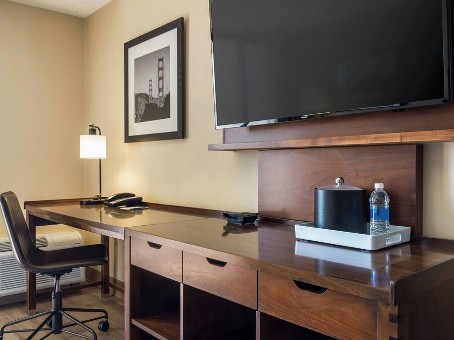 Een hotelkamer met een bureau, stoel, televisie, ingelijst schilderij en een waterfles.