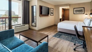 A hotel room with a bed, a desk, a chair, a TV, and a large window with curtains.