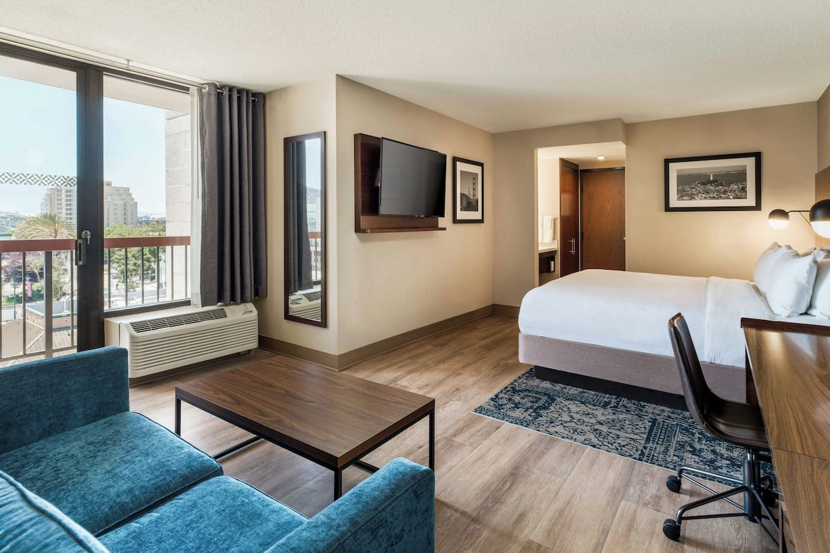 Ein Hotelzimmer mit Bett, Schreibtisch, Stuhl, Fernseher und einem großen Fenster mit Vorhängen.