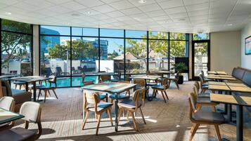 A spacious indoor area with tables and chairs arranged around a pool, large windows offering views of the outside.