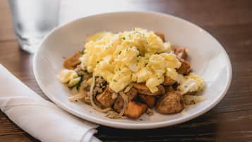 A white plate with scrambled eggs, diced potatoes, and onions on a wooden table.