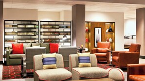 A modern hotel lobby with a sofa, armchairs, a bookshelf, and a wooden cabinet.