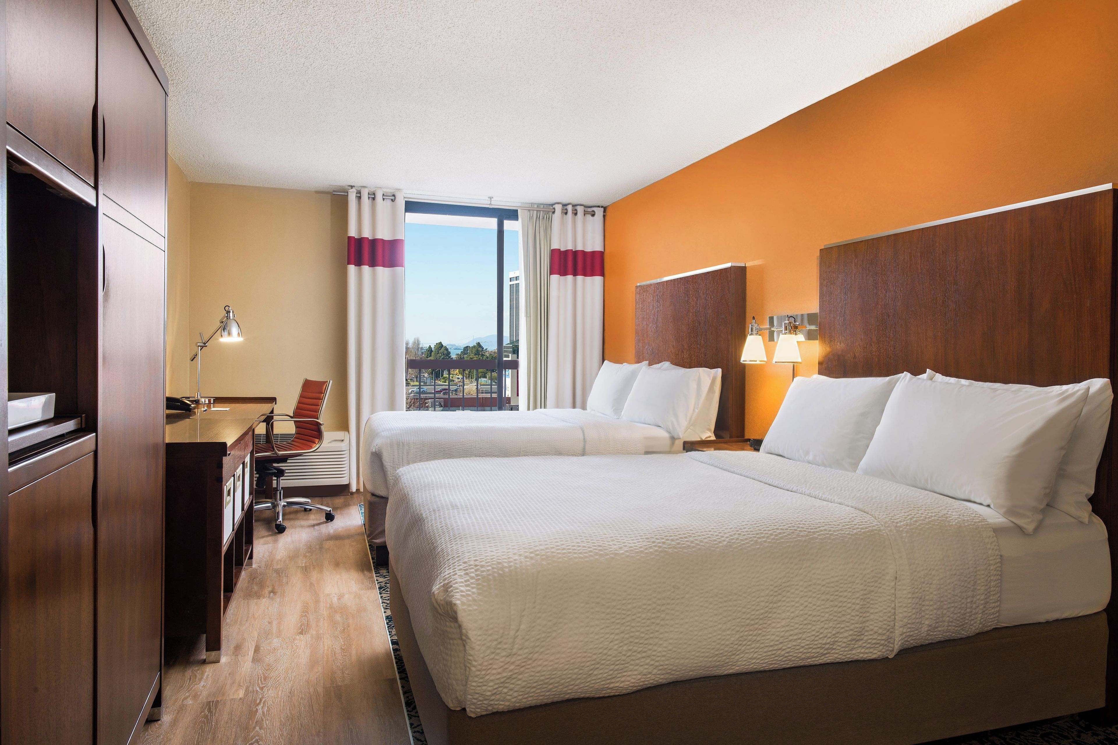 Une chambre d’hôtel avec deux lits, un bureau, une chaise, une lampe et une vue sur la ville.