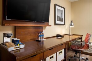 A hotel room with a wooden desk, a flat-screen TV, a coffee machine, bottled water, a chair, and a framed picture on the wall. - Four Points by Sheraton San Francisco Bay Bridge (Emeryville)