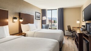 A hotel room with two beds, a desk with a television, a chair, and a window with curtains.