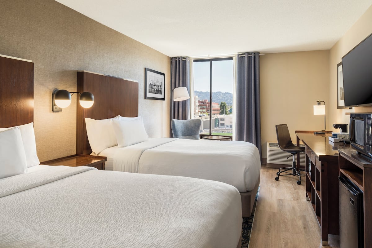 Ein Hotelzimmer mit zwei Betten, einem Schreibtisch mit Fernseher, einem Stuhl und einem Fenster mit Vorhängen.