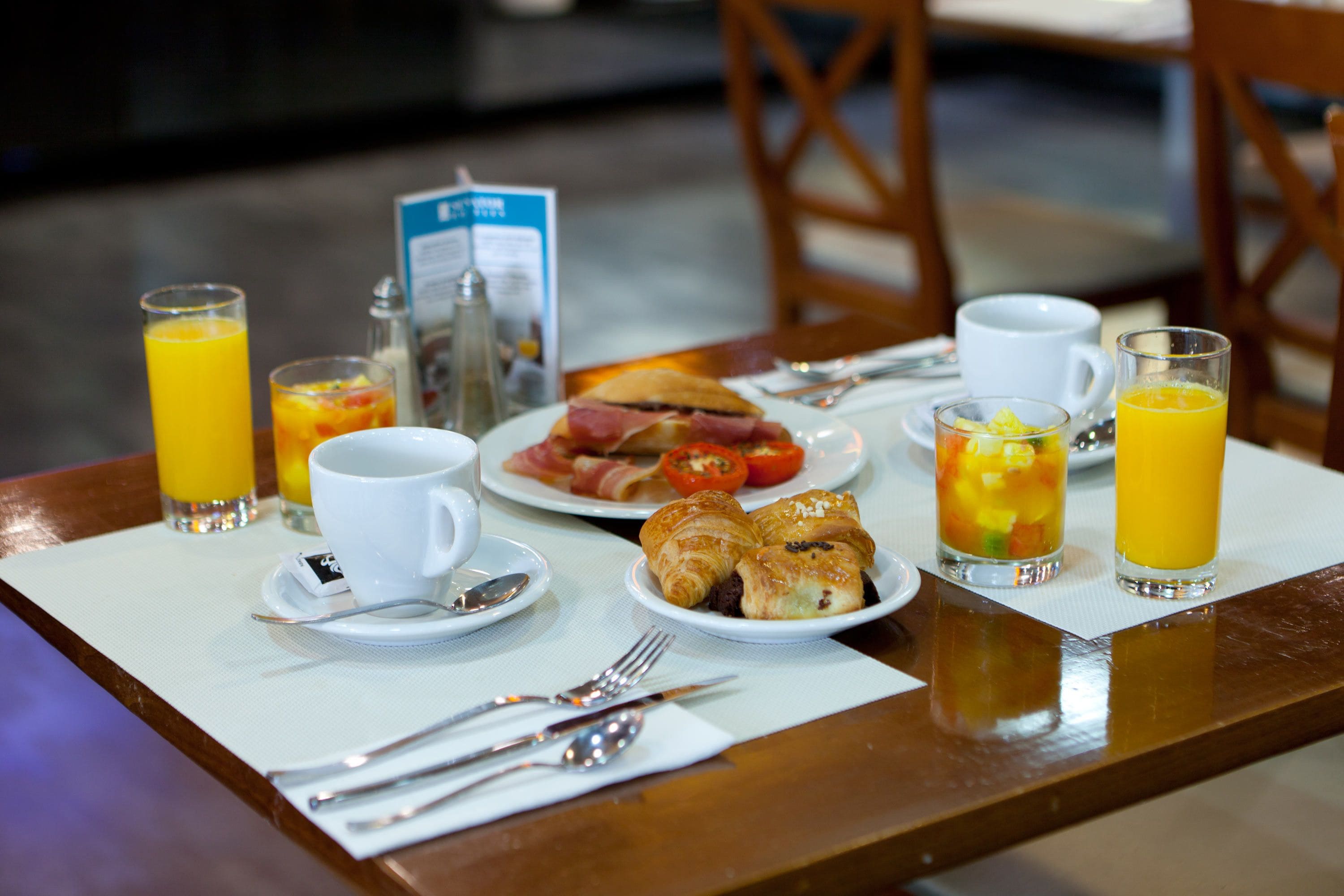 Une table de petit-déjeuner avec des assiettes remplies de nourriture, des verres de jus d’orange et un menu.