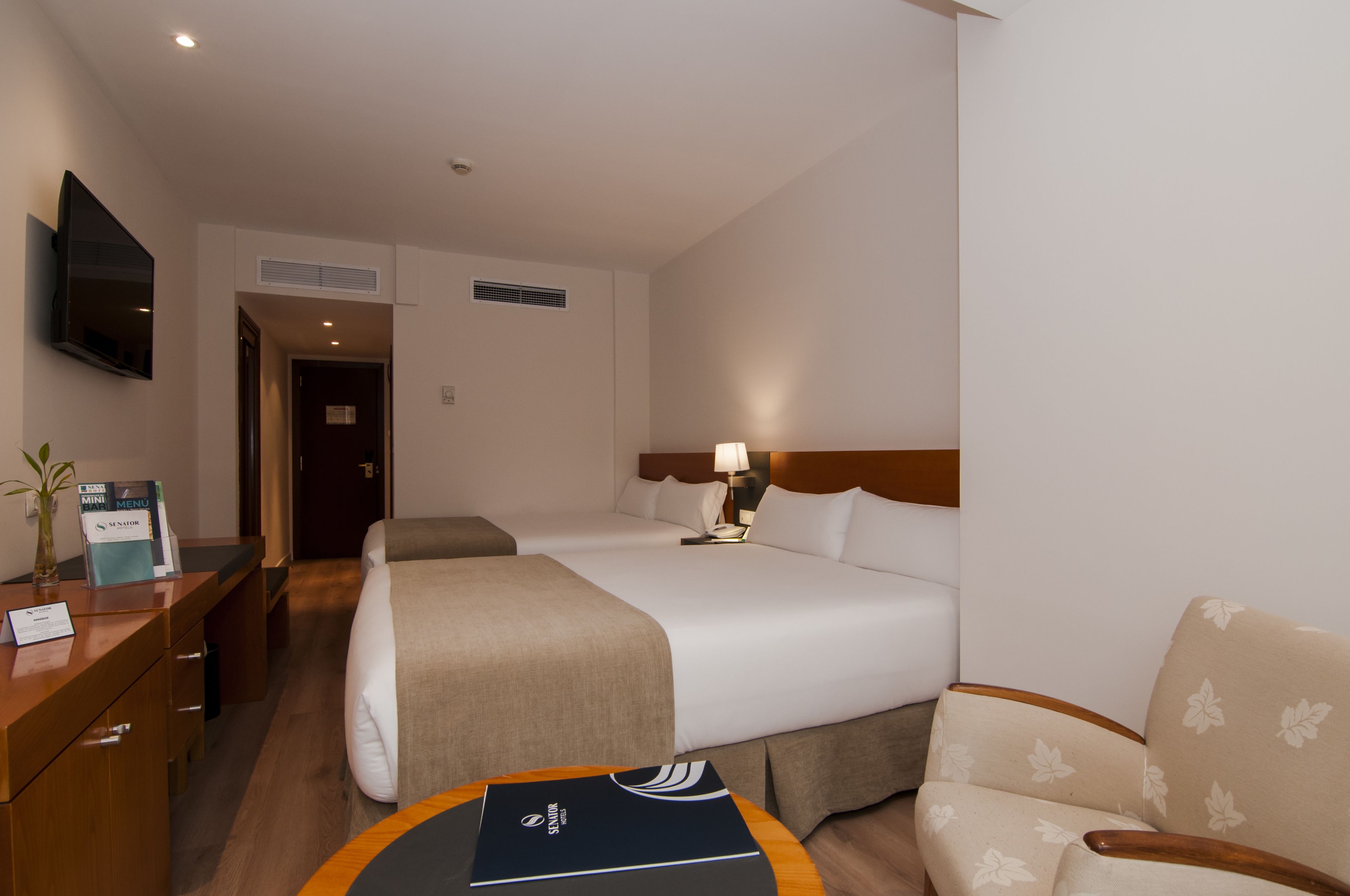 Une chambre d’hôtel avec deux lits, un bureau avec une chaise, un téléviseur fixé au mur et une petite table avec un set de table.