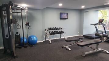 A gym with a weight machine, dumbbells, exercise balls, and a treadmill.