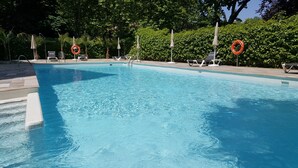 Une piscine d’un bleu éclatant, bordée de chaises longues et d’ombrelles, et entourée de verdure.