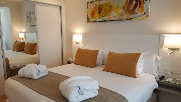 Une chambre d’hôtel avec un grand lit, deux oreillers, une table de chevet avec une lampe, un miroir et un tableau au mur.