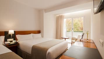 Habitación de hotel con una cama grande, mesita de noche con lámpara, una pequeña mesa redonda, una silla y un televisor en la pared.