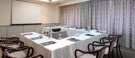 A conference room with a long table, chairs, a projector screen, and a curtain.