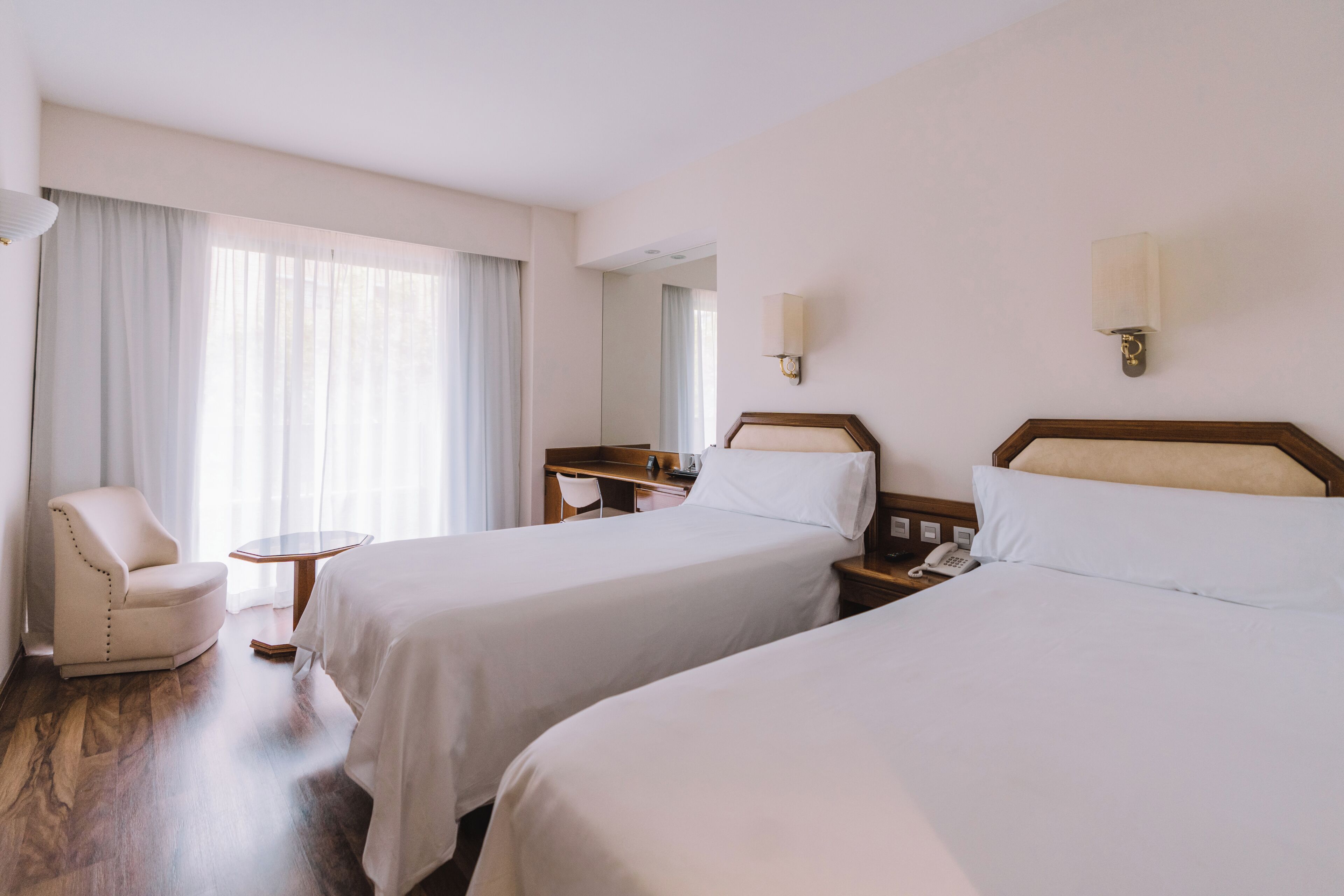 Una habitación de hotel con dos camas, un escritorio, una silla, una lámpara y un espejo.