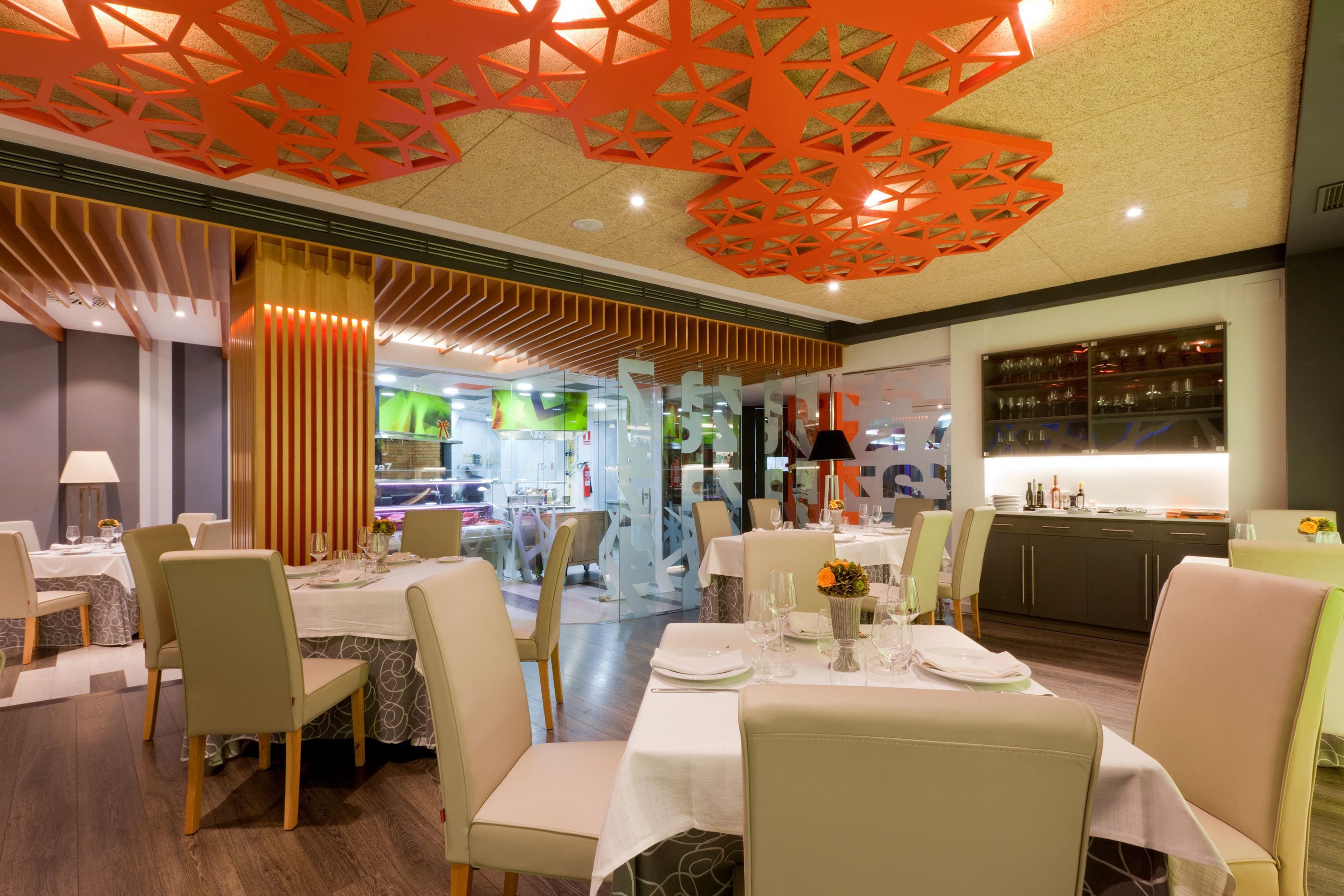 Restaurante com mesas preparadas para refeições, área de cozinha e teto decorativo.