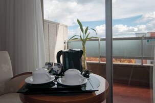 A balcony with a table set for two, a coffee maker, a plant, and a view of the cityscape.