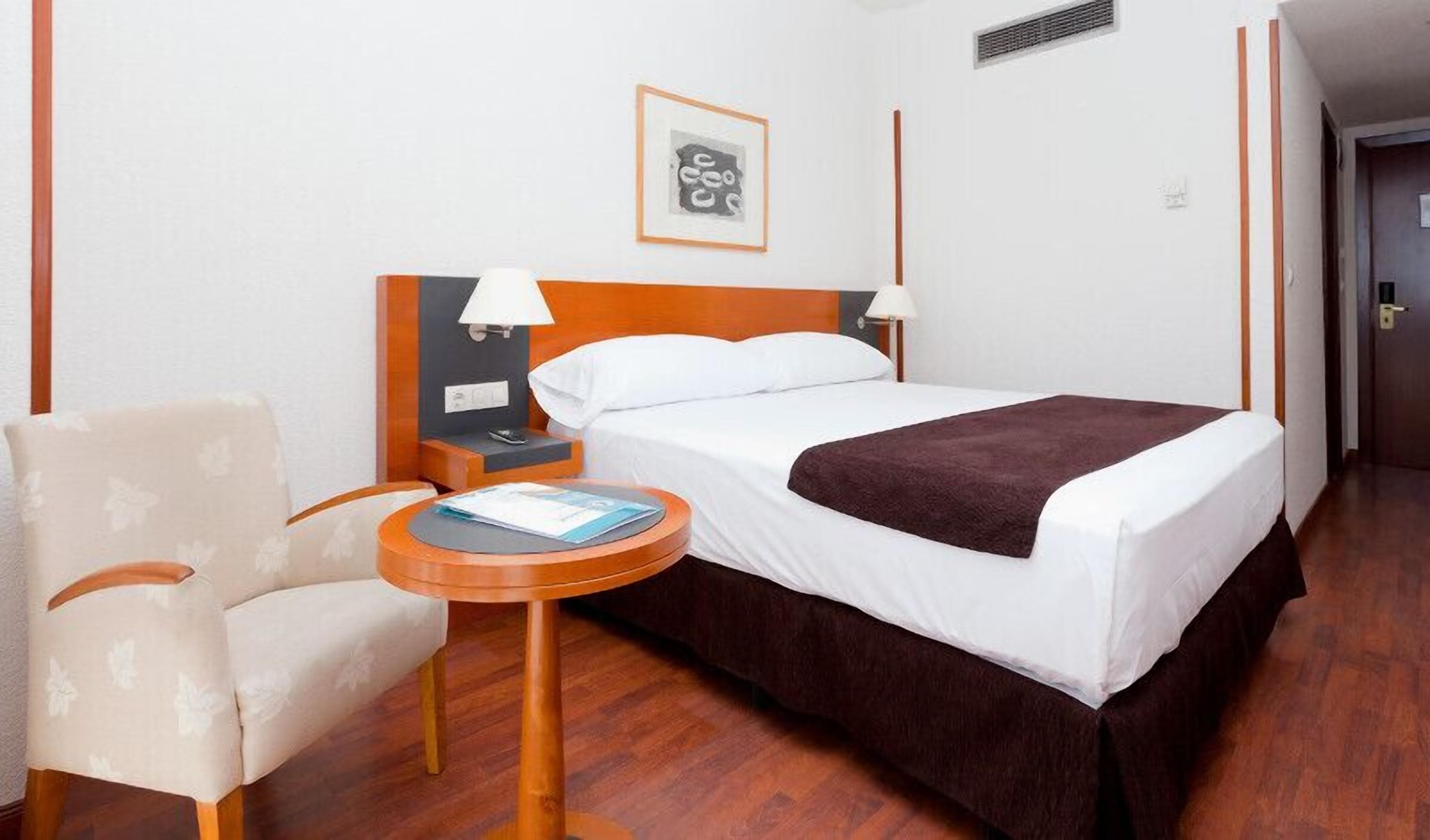 Ein Hotelzimmer mit Bett, Sessel, kleinem Tisch und einem Bild an der Wand.