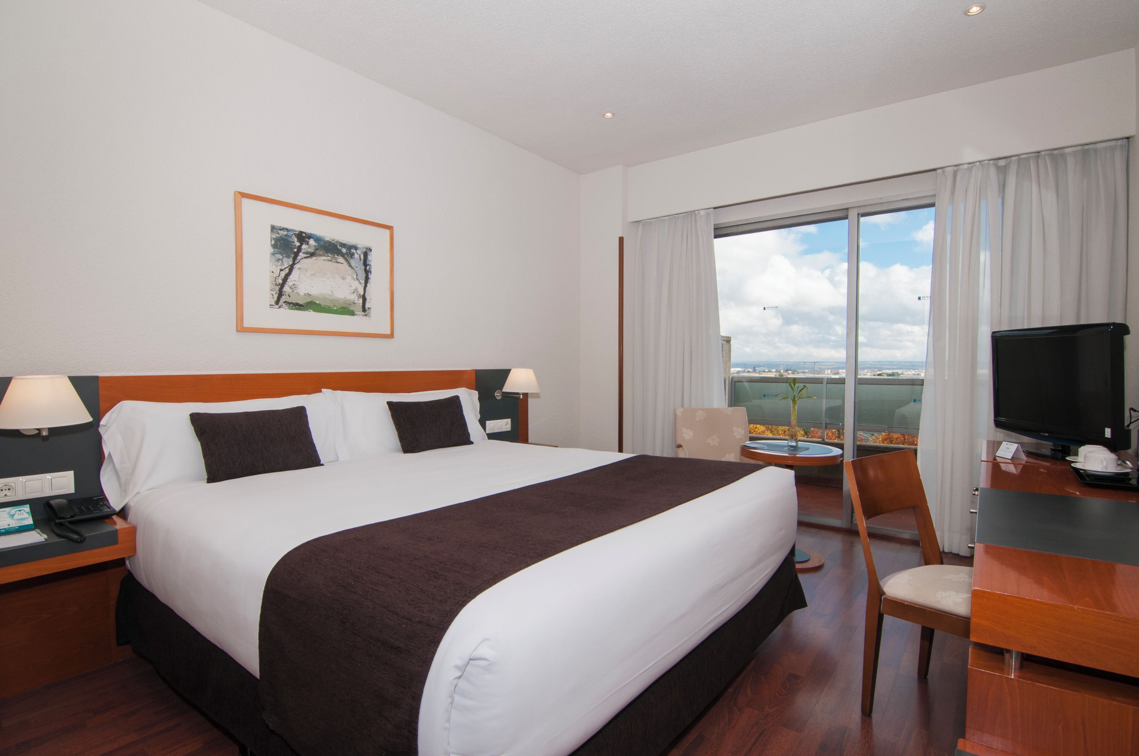 A hotel room with a bed, a desk, a chair, a TV, and a window with a view.