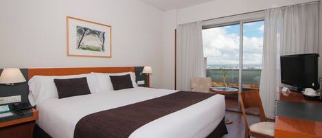 A hotel room with a bed, a desk, a chair, a TV, and a window with a view.