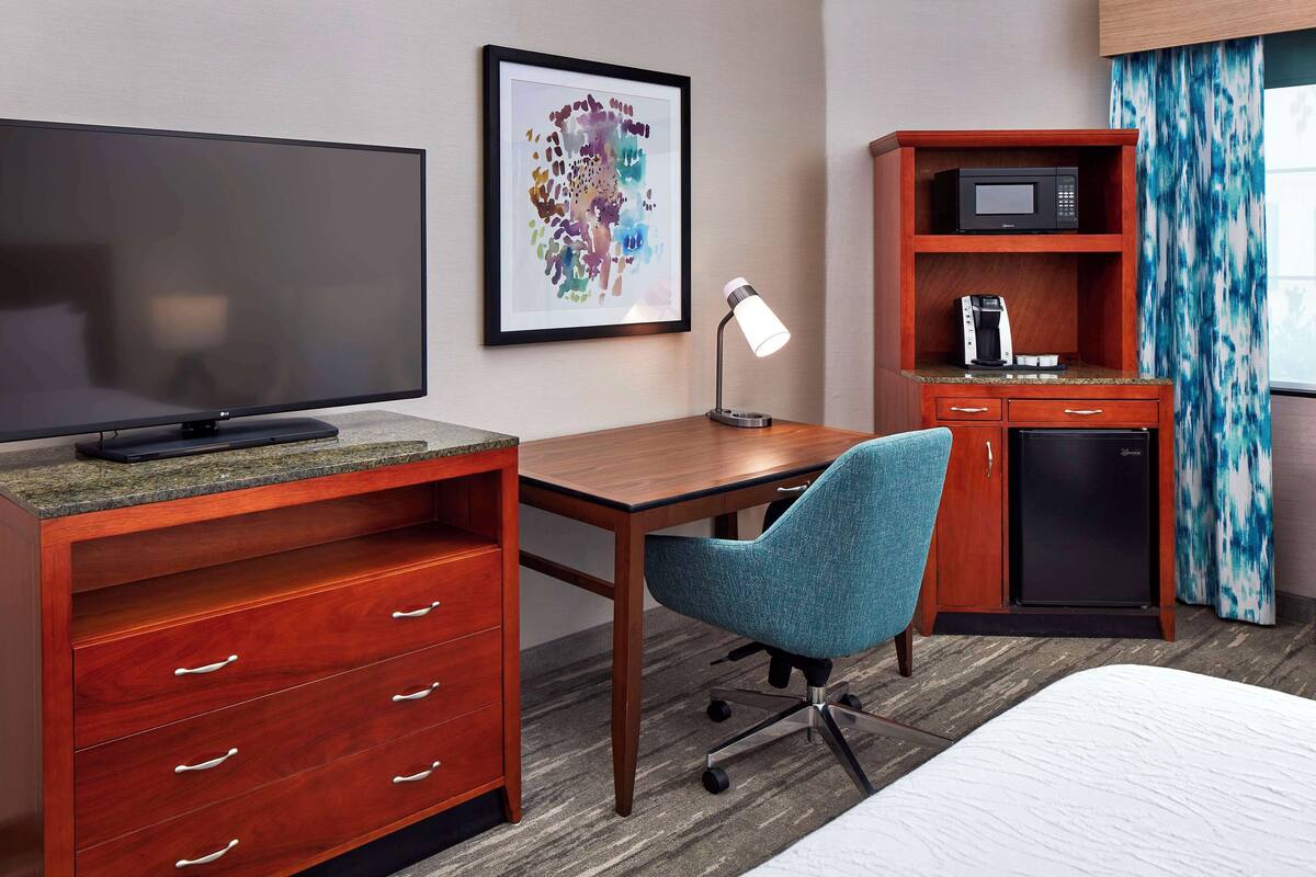A hotel room with a flat-screen TV, a desk with a chair, a coffee maker, a microwave, and a small refrigerator.