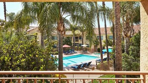 A pool area with lounge chairs and umbrellas, surrounded by palm trees and a building with a tiled roof. - Hilton Garden Inn Valencia Six Flags (Valencia)