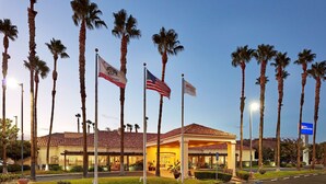 A hotel with a covered entrance, palm trees, and flags. - Hilton Garden Inn Valencia Six Flags (Valencia)