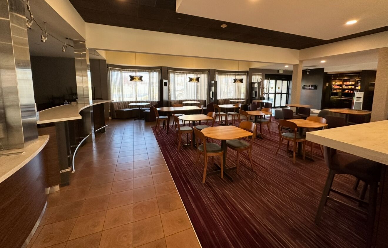 A modern restaurant with a mix of booths and tables, a kitchen area, and a visible market sign.