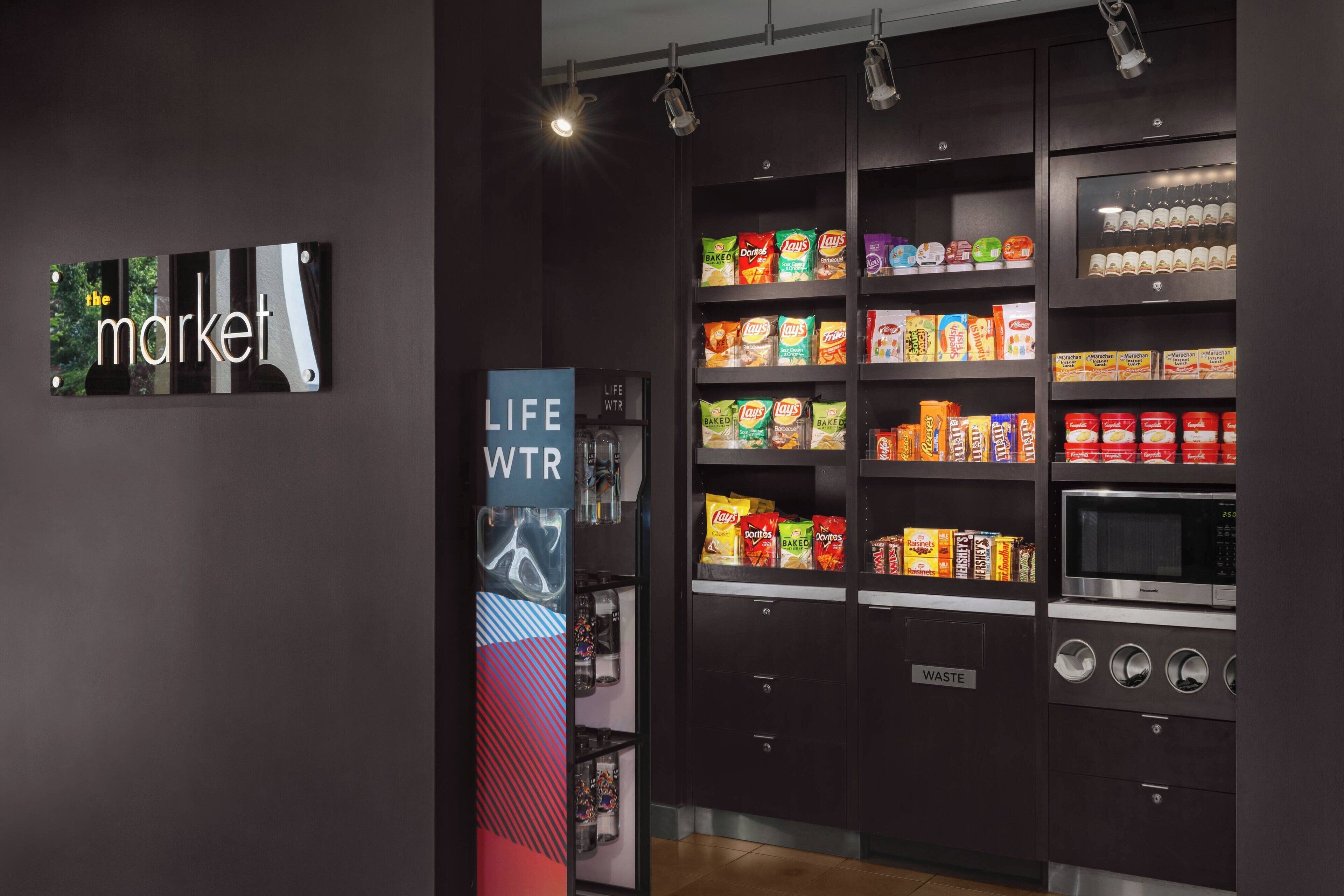 A vending machine area with snacks and a microwave, labeled 'WASTE'.