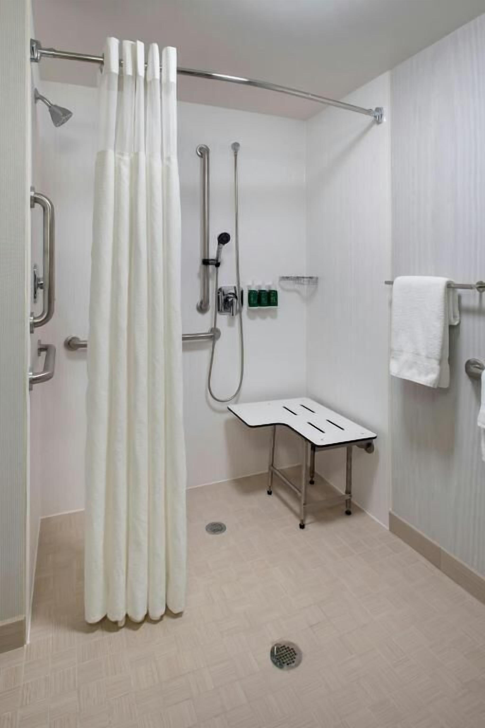 A bathroom with a shower, grab bars, a bench, and a towel rack.