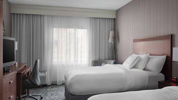 A hotel room with two beds, a desk with a chair, a television, and a lamp.