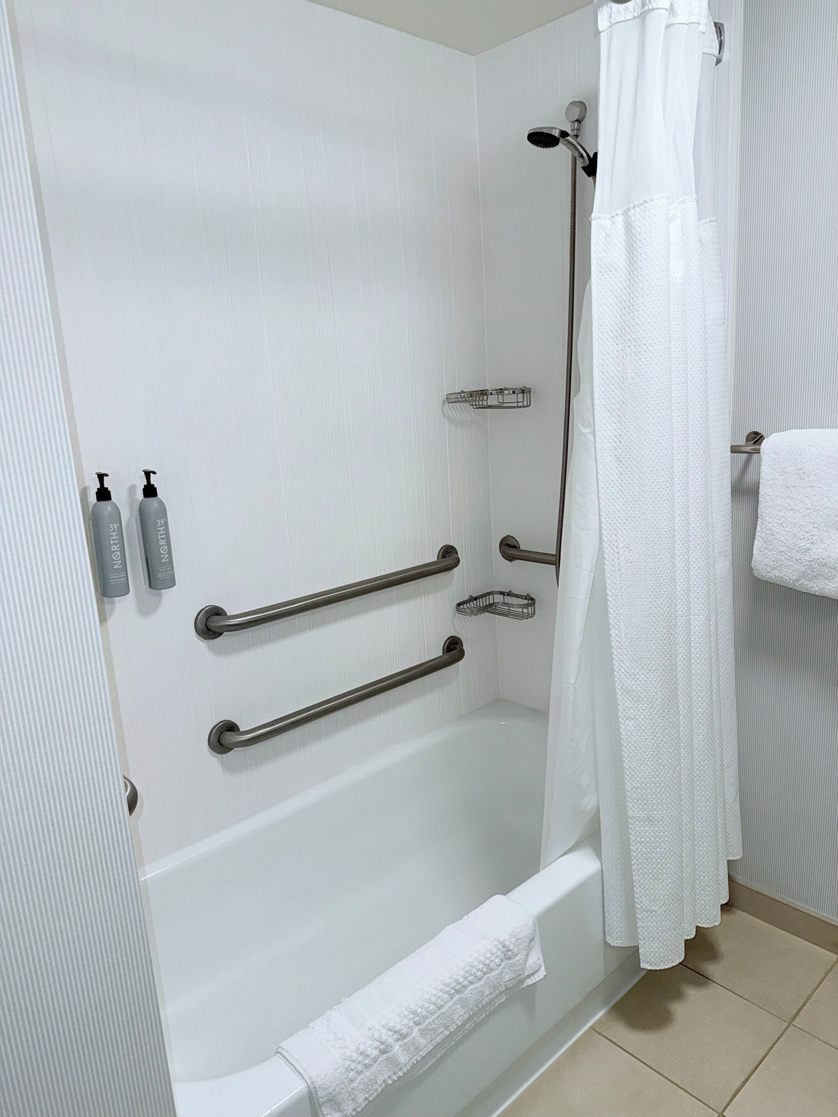 A bathroom with a white bathtub, grab bars, a shower curtain, and a towel rack.
