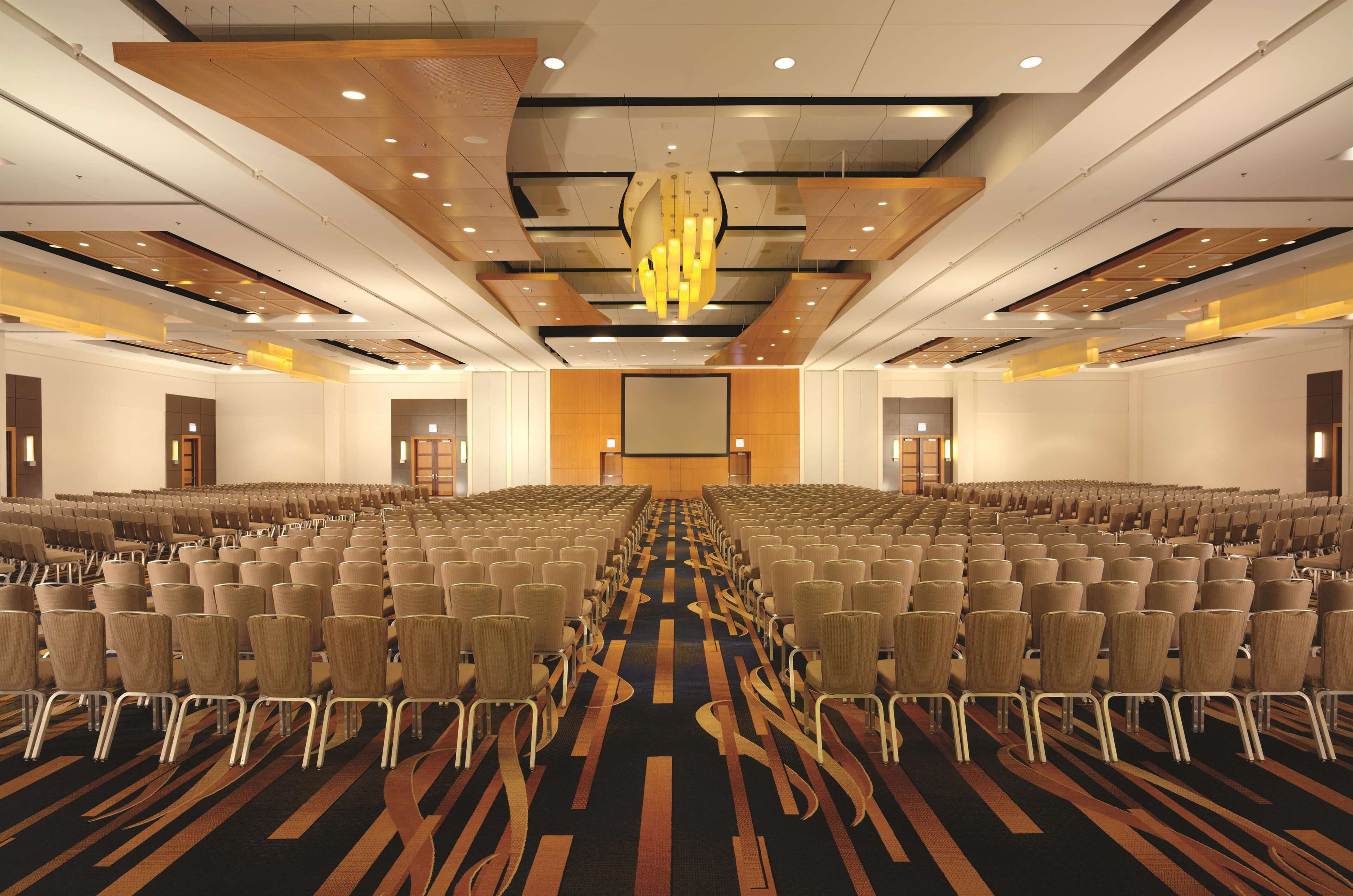 Un salón de conferencias con filas de sillas, una pantalla grande y una lámpara de araña moderna.