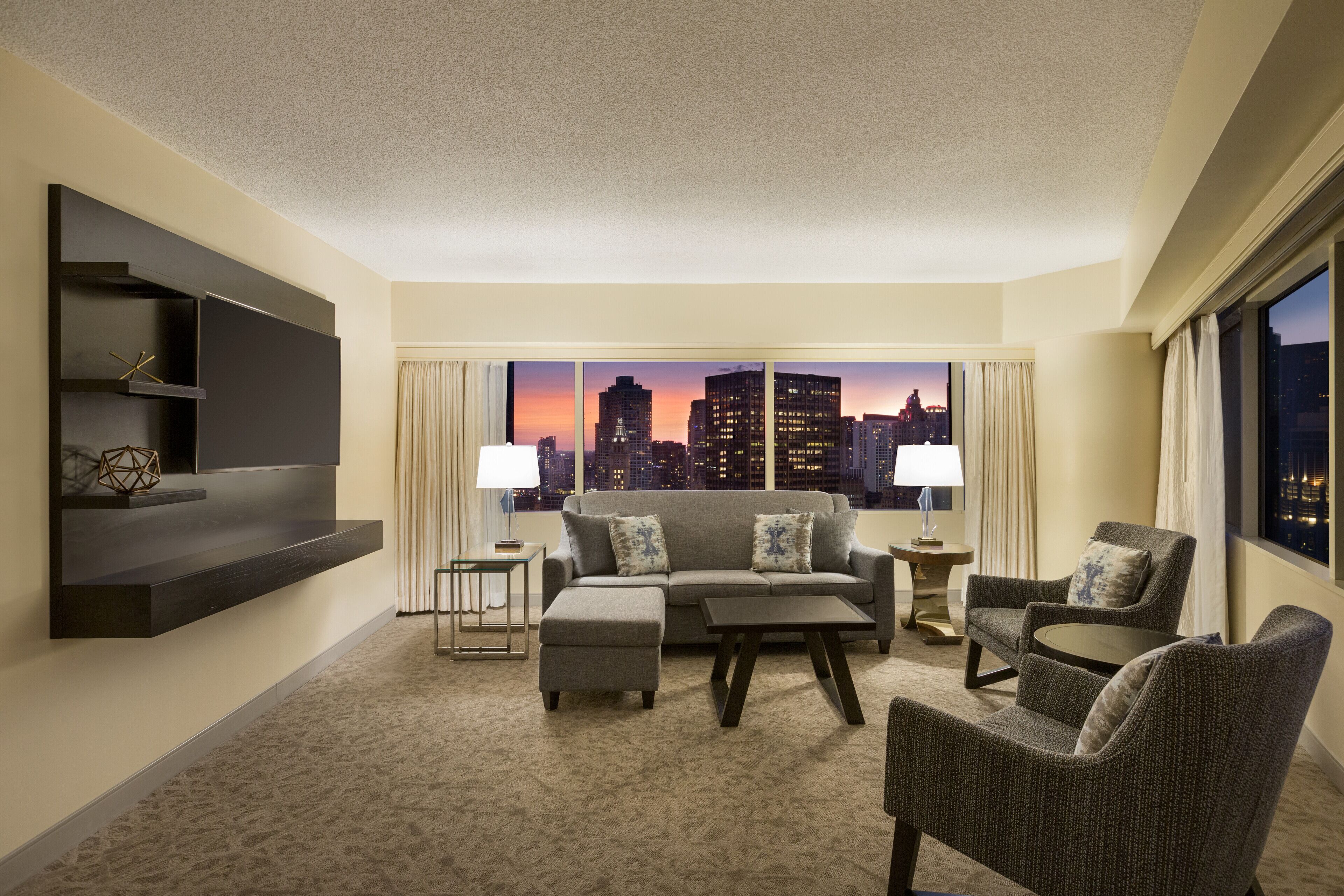 Habitación de hotel moderna con vistas a la ciudad, un sofá, una mesa de centro y una silla.