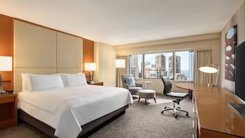 Habitación de hotel con una cama grande, un escritorio, dos sillas, un televisor y vistas a la ciudad.