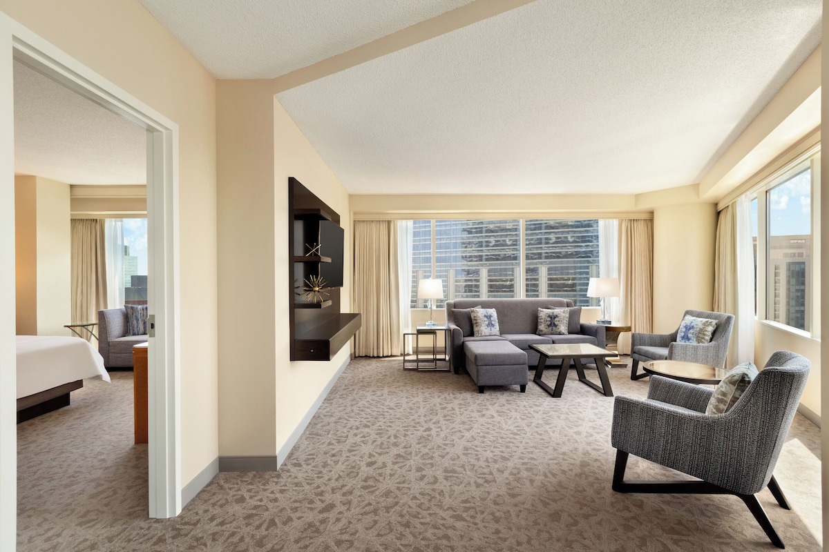 A hotel room with a large bed, a sofa, a chair, a small table, and a TV on a stand.