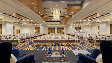 A conference room with rows of tables and chairs, a central podium, and a modern chandelier.
