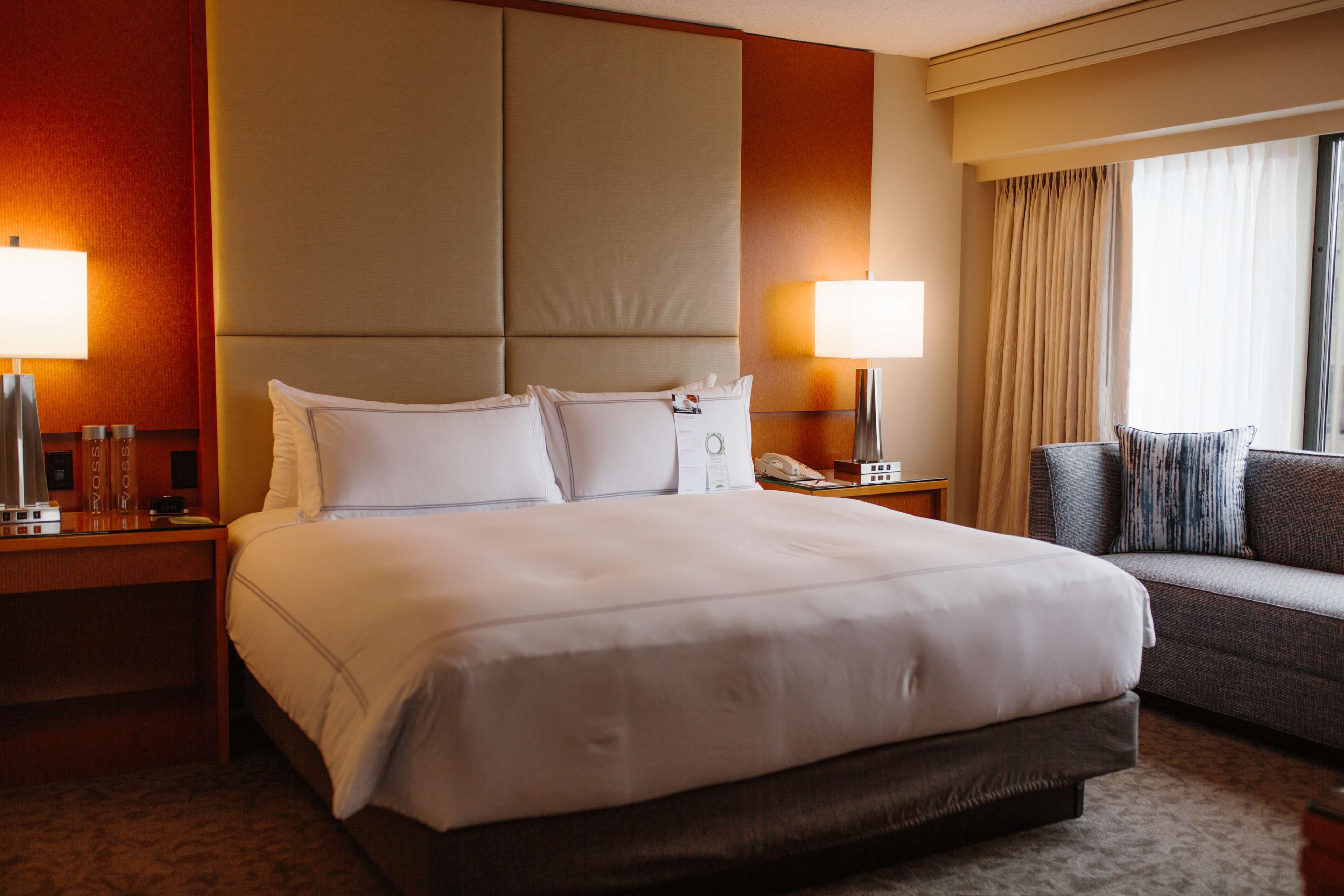 A hotel room with a large bed, a sofa, two bedside tables with lamps, a telephone, and a window with curtains.