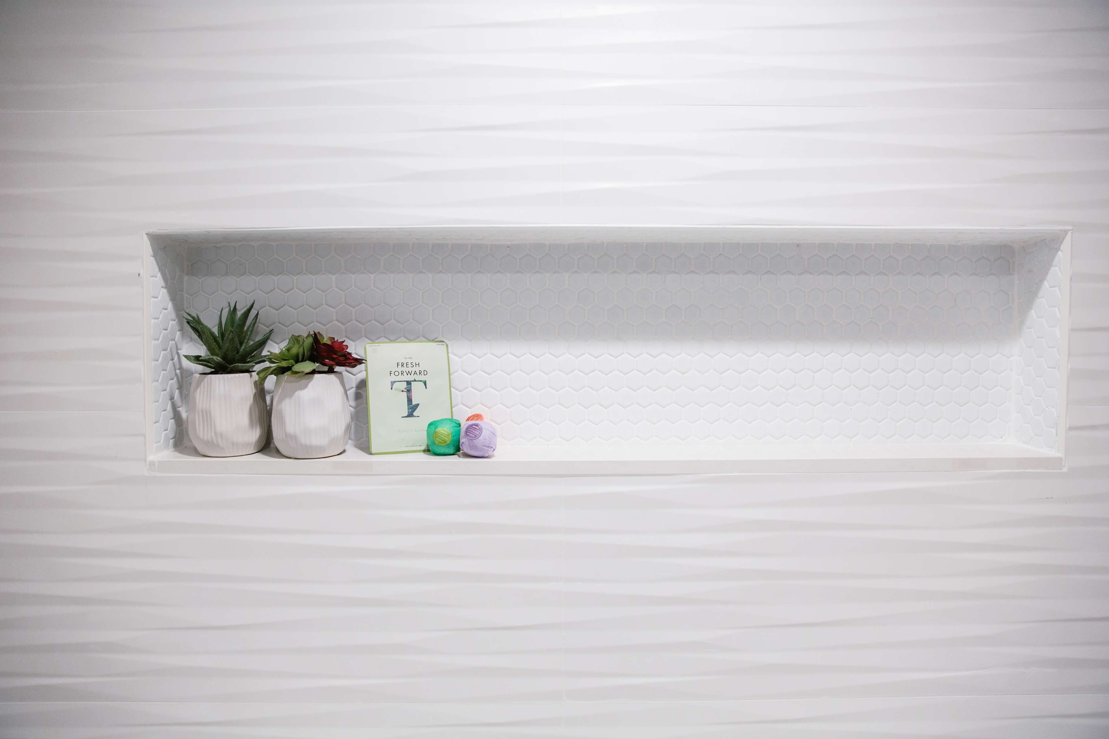 A white shelf with two potted plants and a book titled "FRESH FORWARD" against a white textured wall.