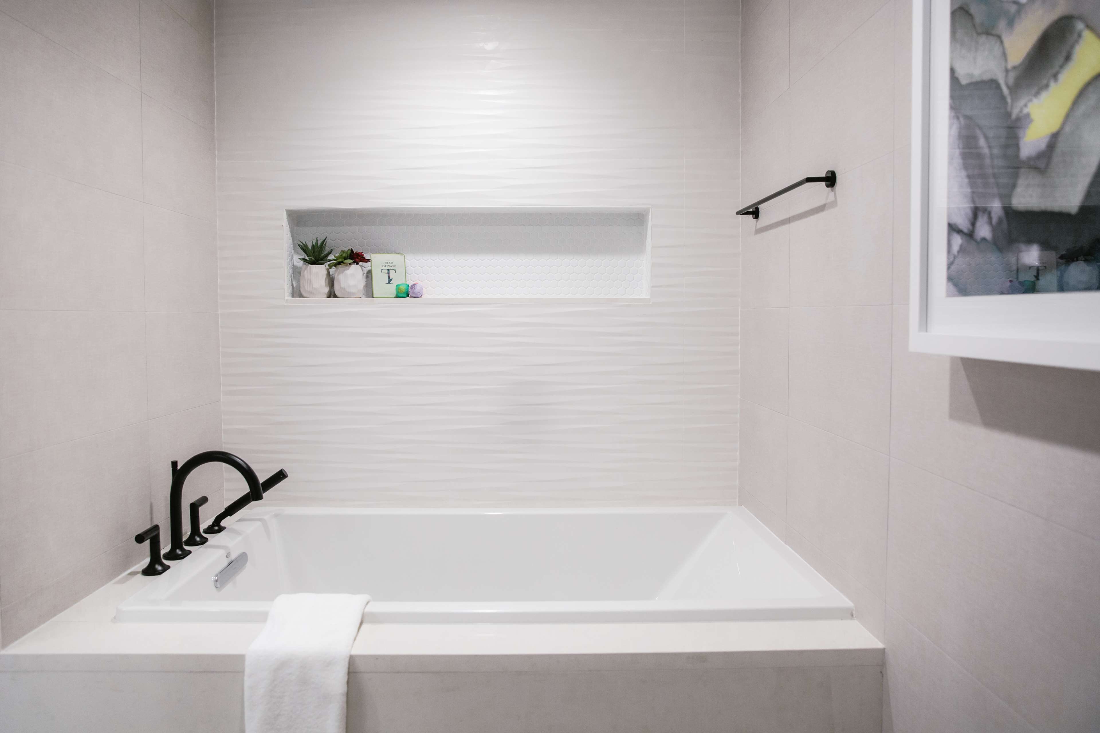 A modern bathroom with a white bathtub, a shelf with toiletries, and a framed picture on the wall.