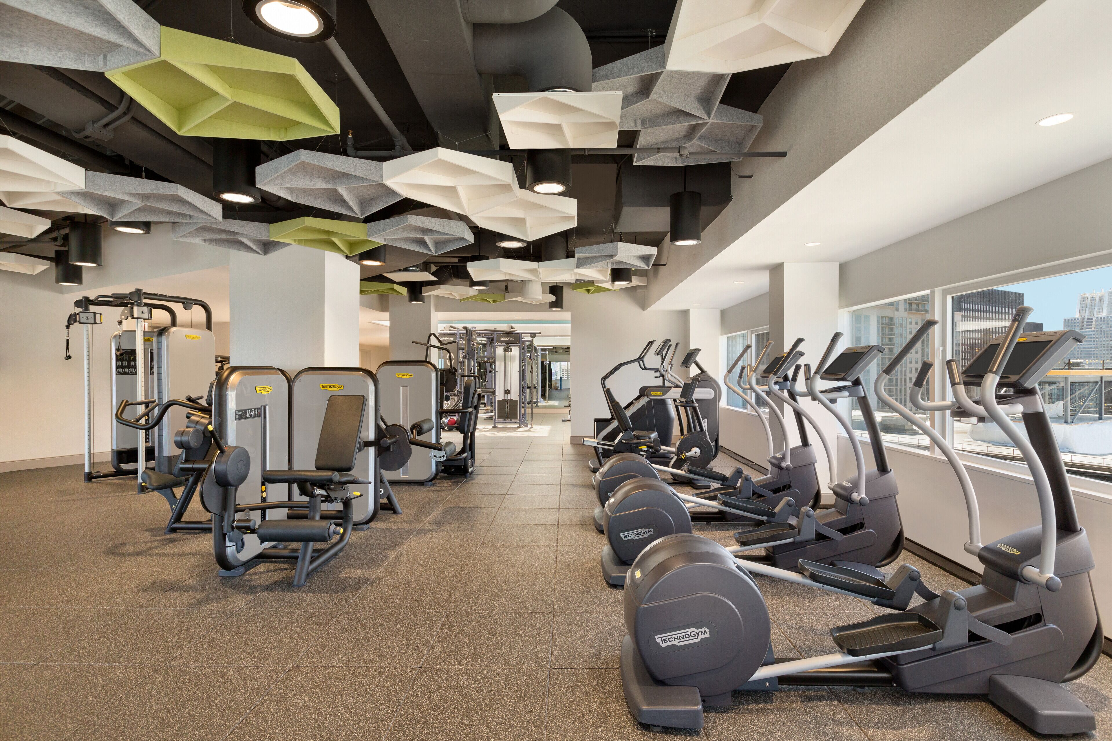 Un gimnasio con diversas máquinas de ejercicio, incluyendo cintas de correr y máquinas de pesas, dispuestas en filas.