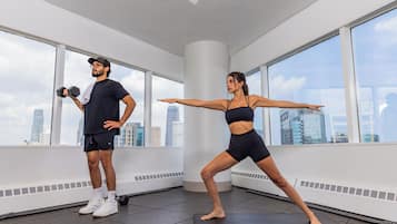 Twee personen aan het sporten in een ruimte met grote ramen en uitzicht op de stad.